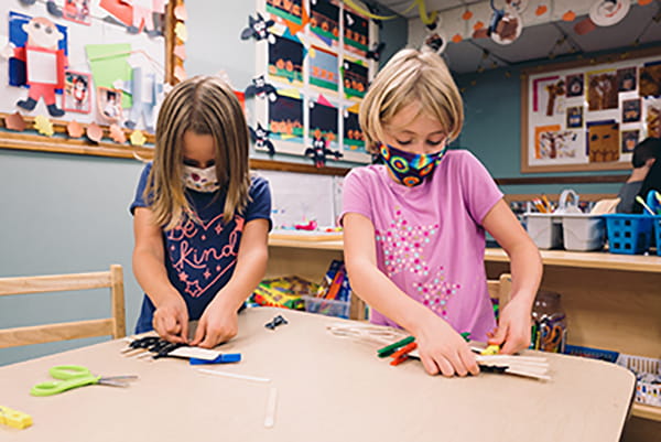 Two young girls work on projects in their classroom.